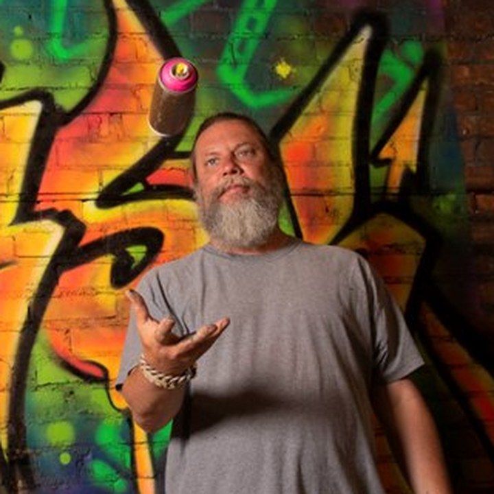 Kelly “RISK” Graval in front of a RISK graffiti wall